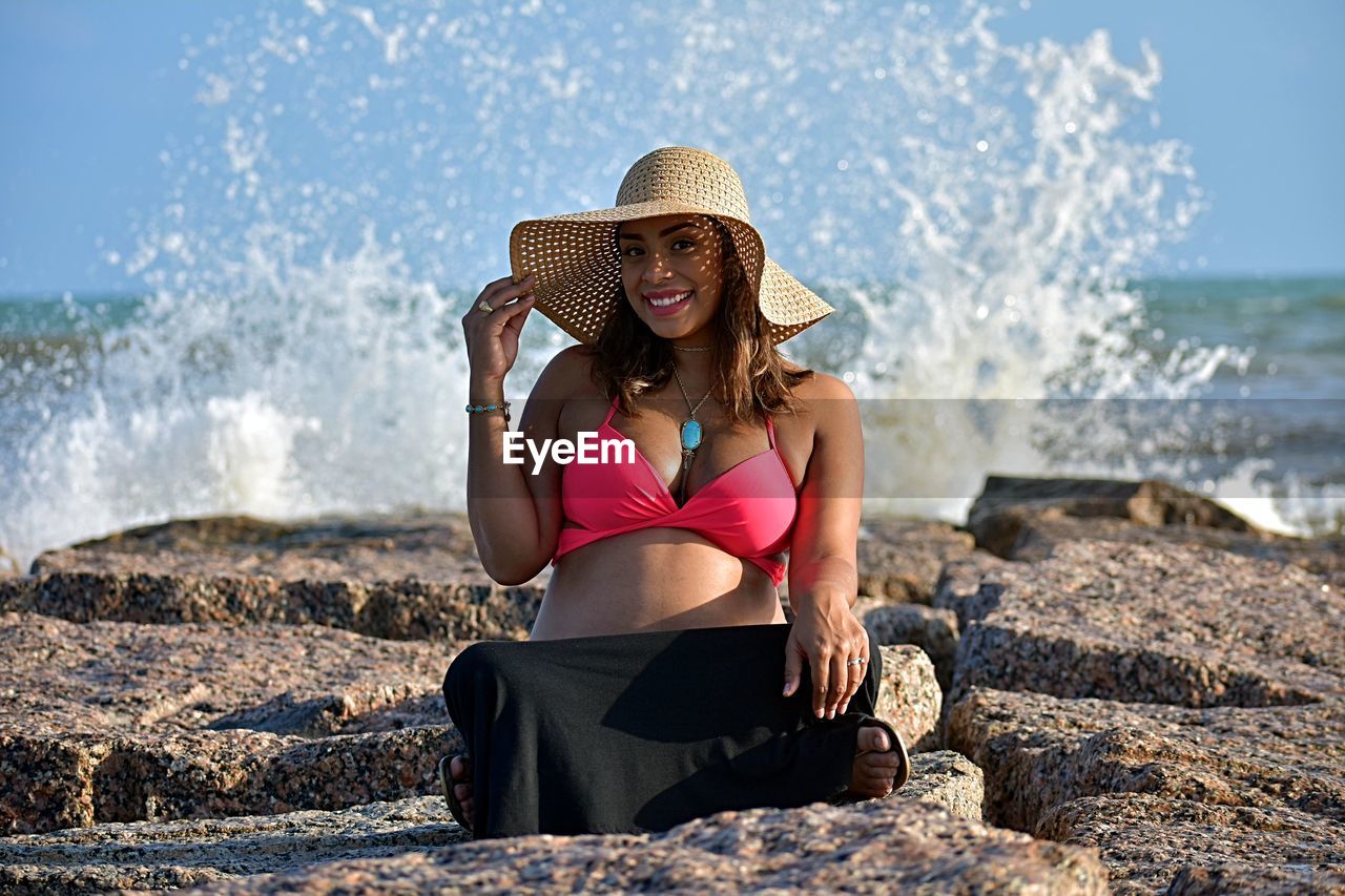 Portrait of mid adult woman sitting on rocks at beach against sky