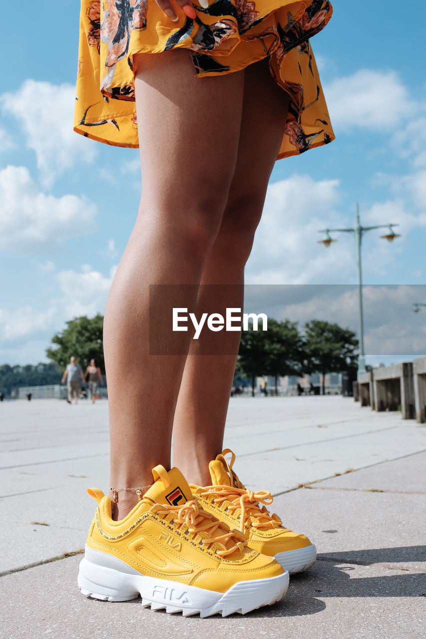 Low section of woman in yellow sports shoes standing on walkway