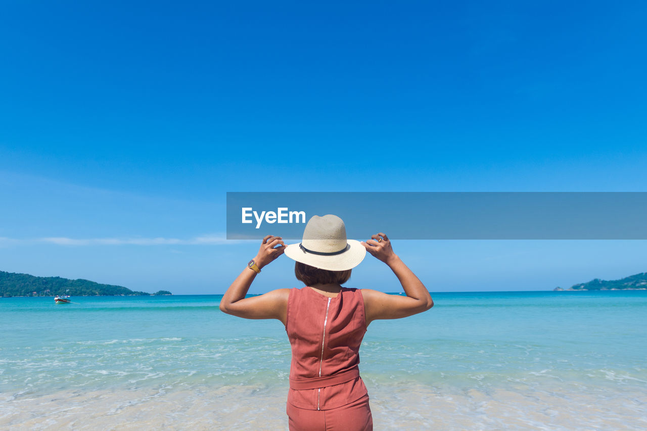 REAR VIEW OF MAN LOOKING AT SEA