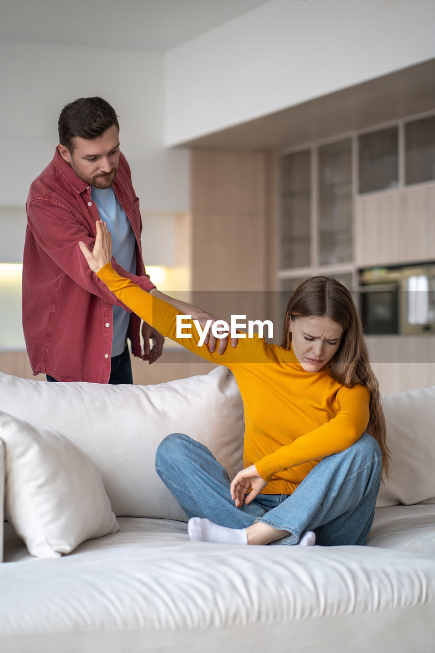 young woman using phone while sitting on bed at home