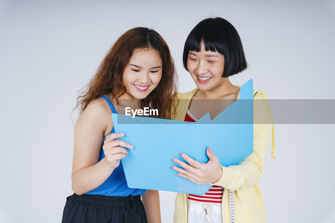 Smiling lesbian couple looking at file against gray background