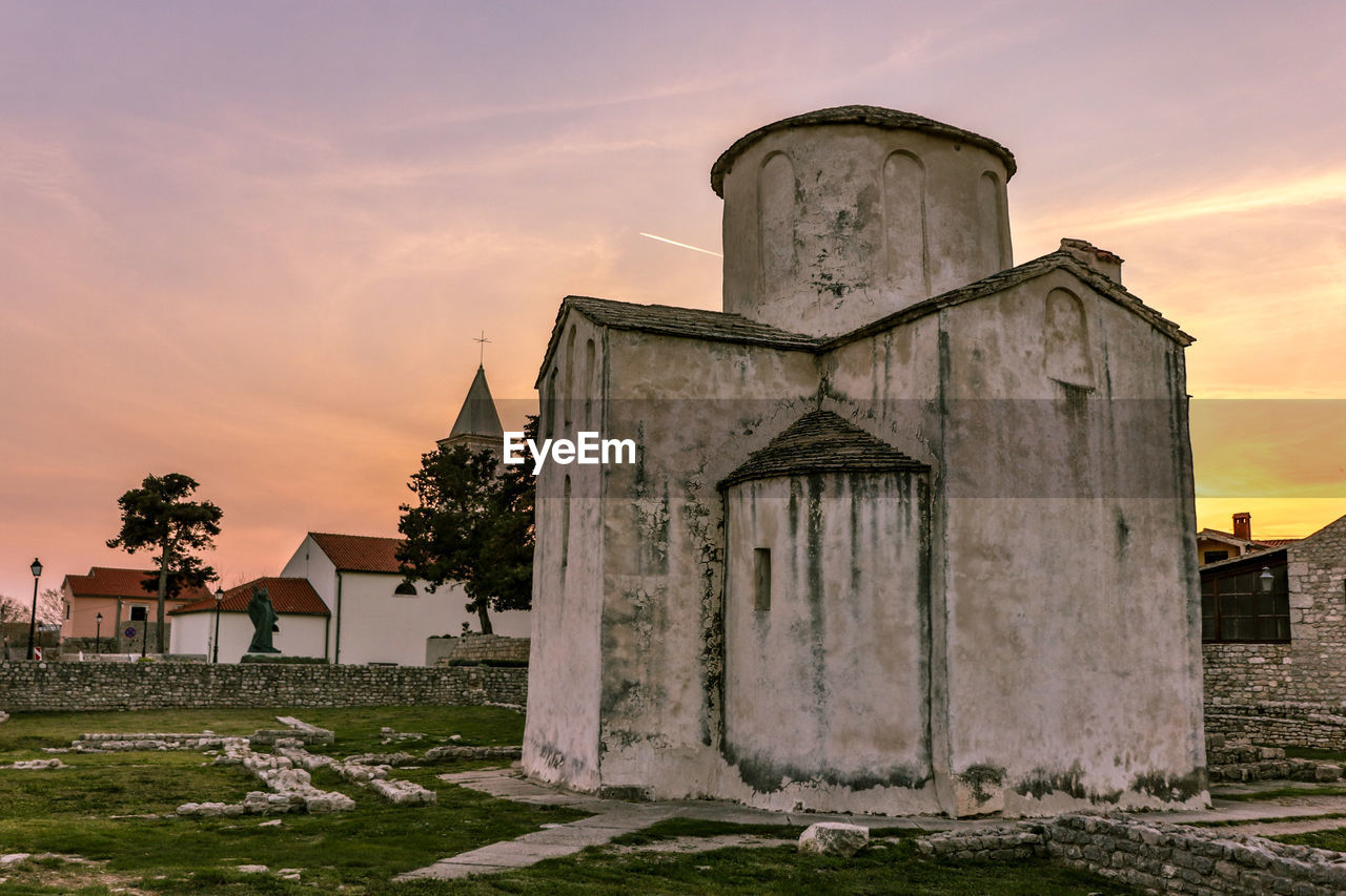 Exterior of old church on field against sky during sunset