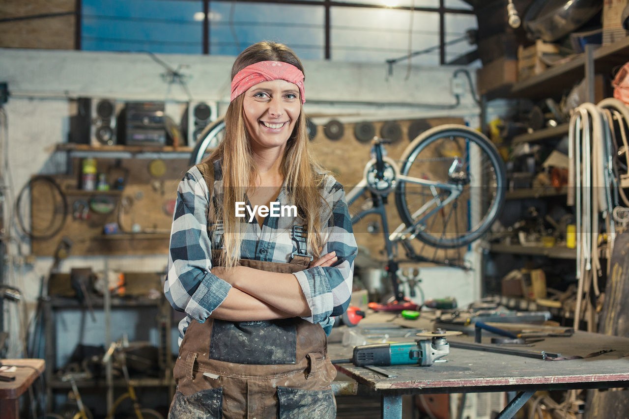 PORTRAIT OF A SMILING YOUNG WOMAN WITH BICYCLE STANDING AGAINST THE WALL