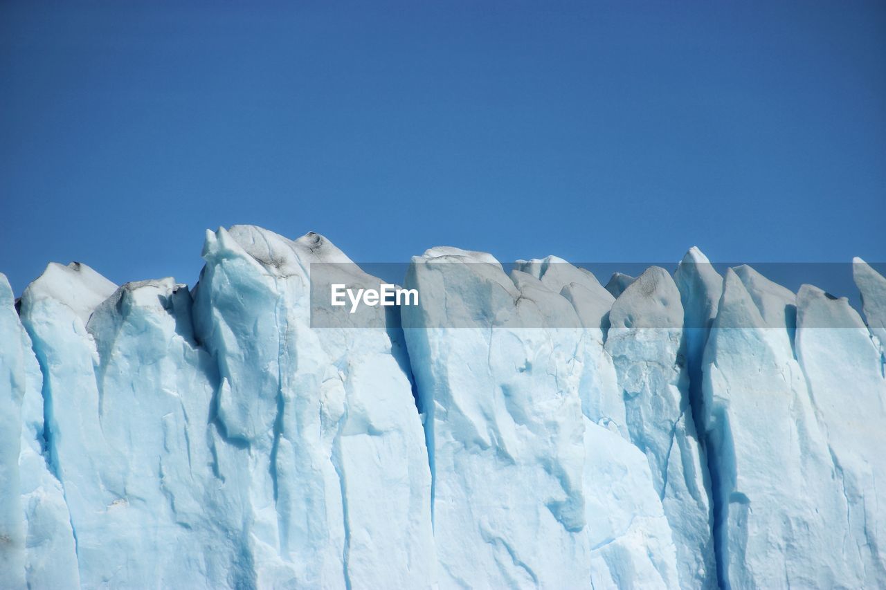 Low angle view of glacier against clear blue sky