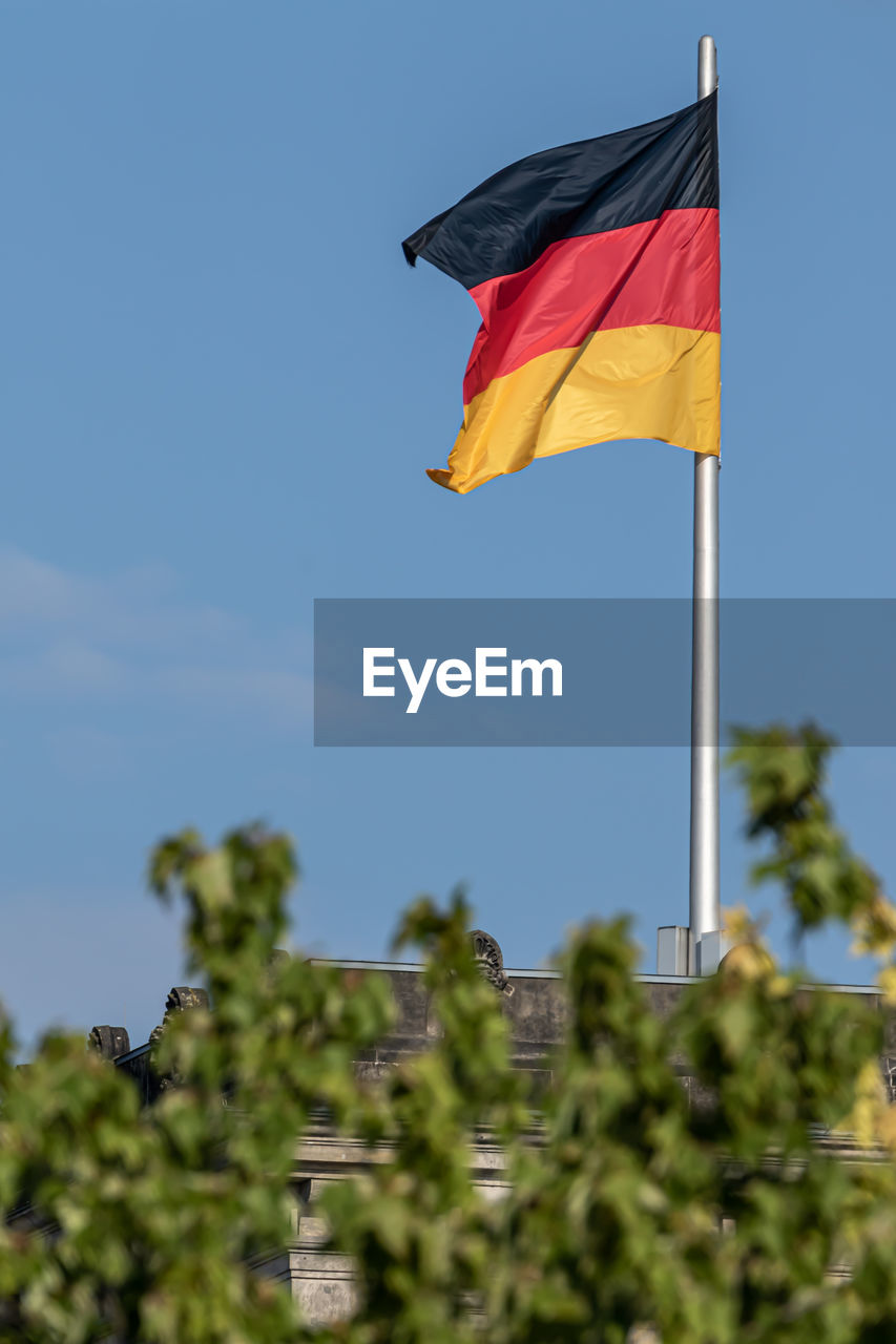 flag, patriotism, nature, sky, environment, wind, day, plant, no people, blue, tree, outdoors, red, yellow, flower, low angle view, sunny, clear sky, pride, multi colored, emotion, green