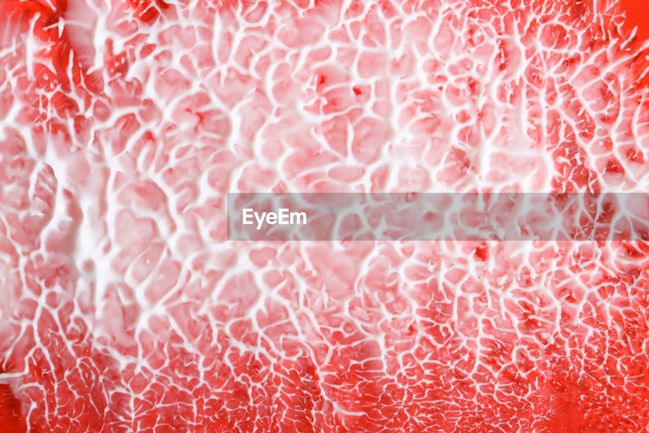 Creamy texture on a red background, top view. white cosmetic strokes and smears of different size