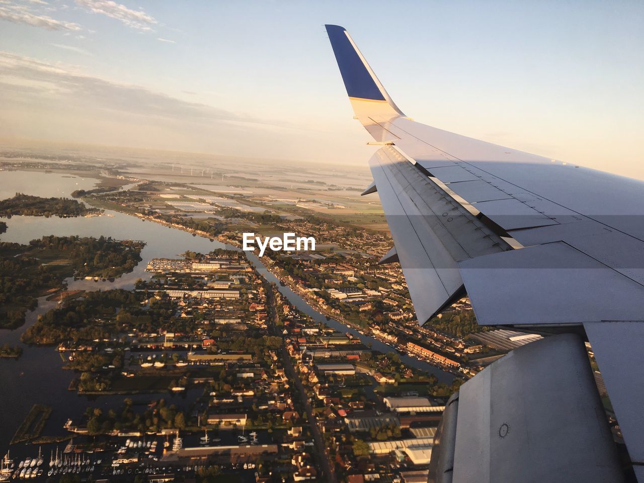 Cropped image of airplane wing flying over city during sunset