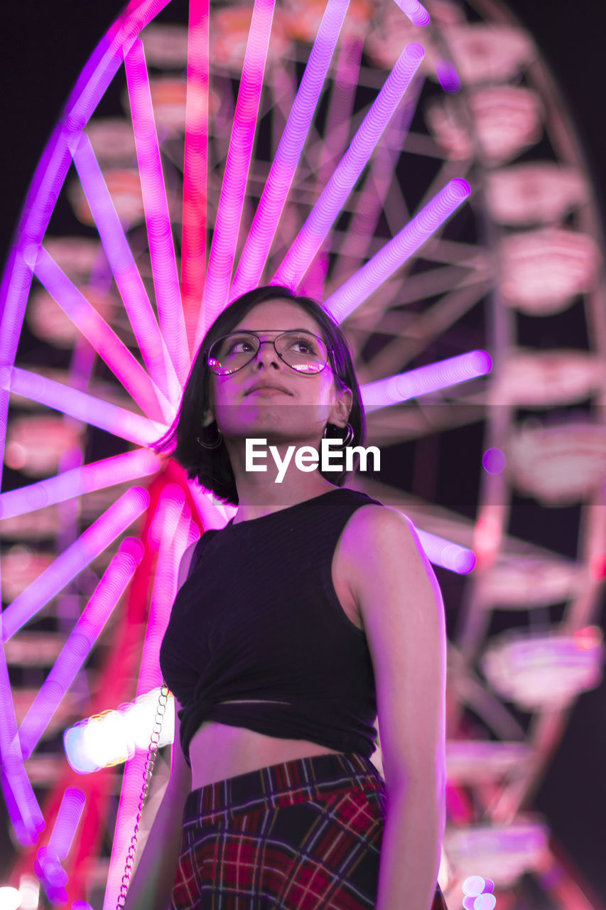 Woman standing by illuminated ferris wheel at night