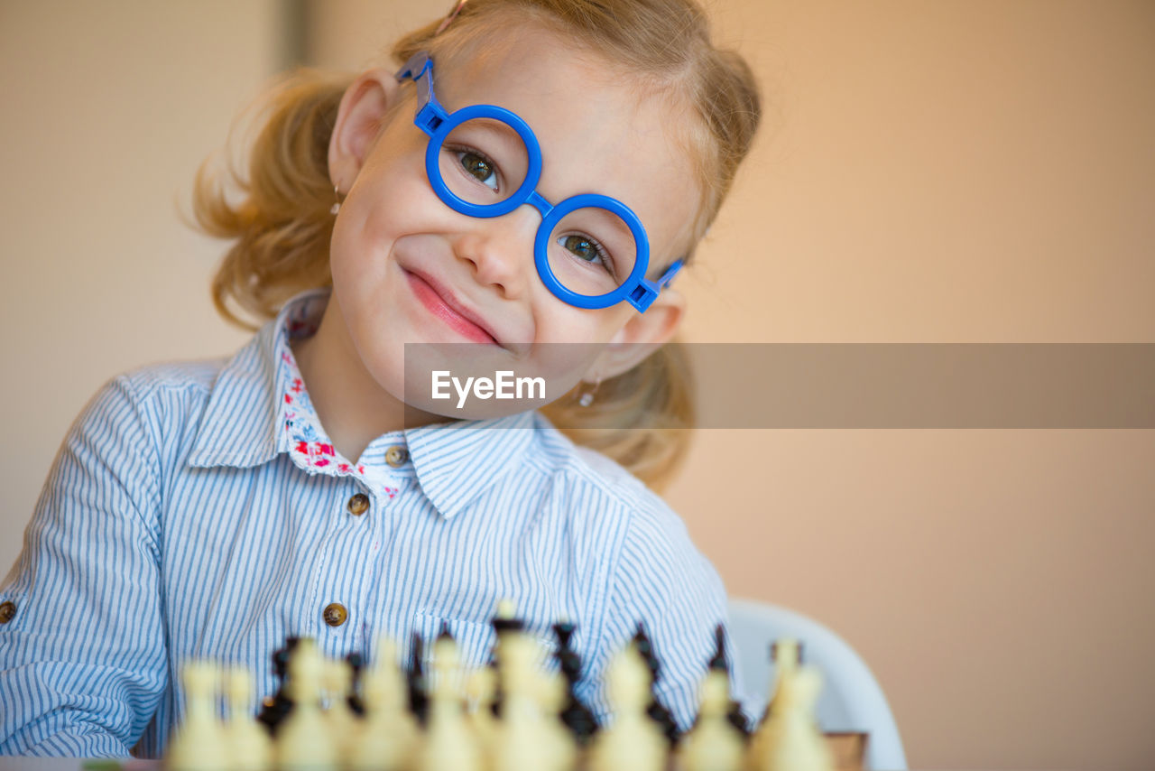 Portrait of smiling girl wearing eyeglasses standing by wall