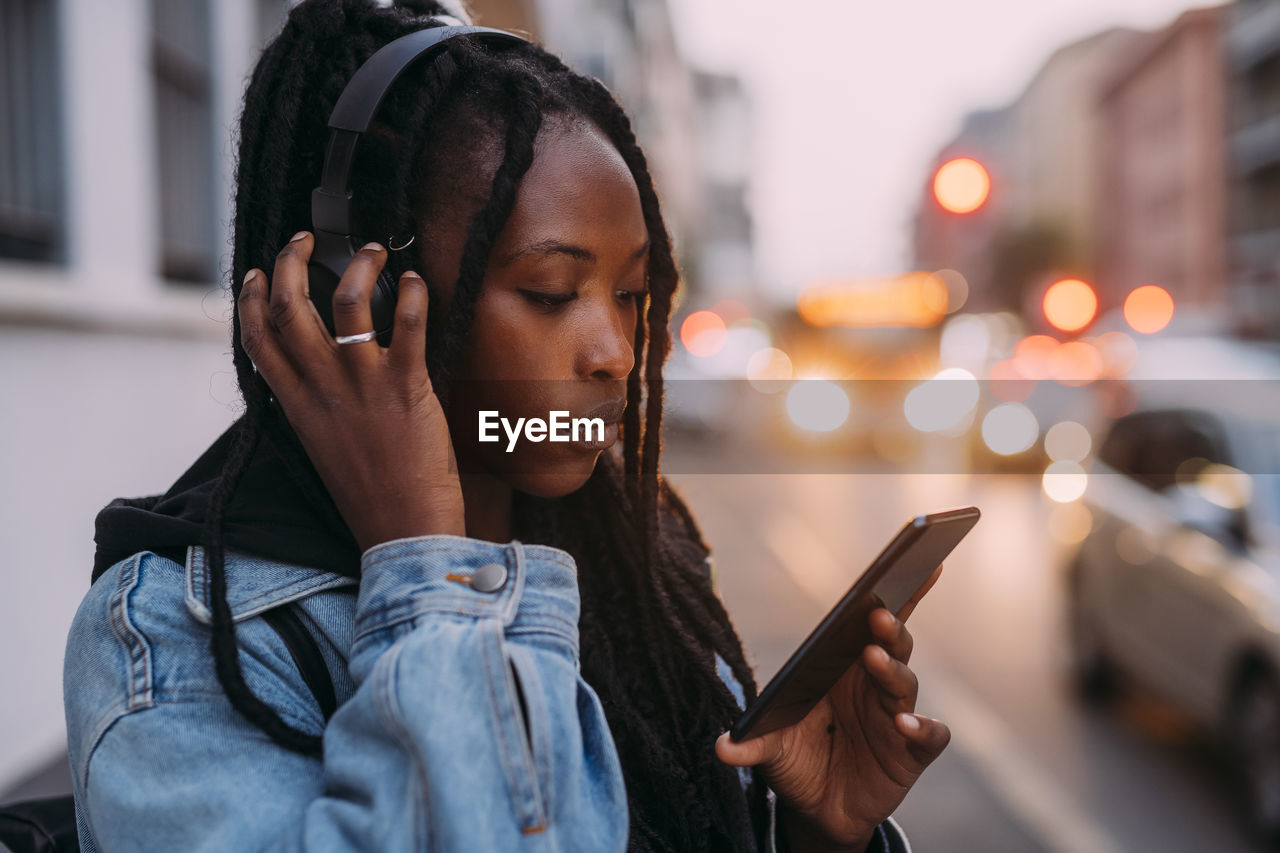 Woman with mobile phone adjusting headphones on road