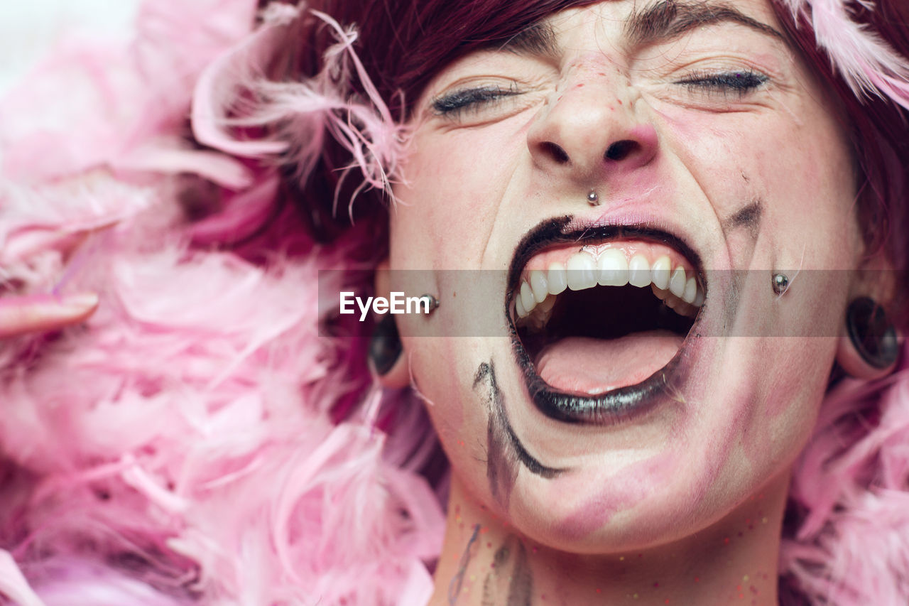 Close-up of woman with make-up screaming amidst pink feathers