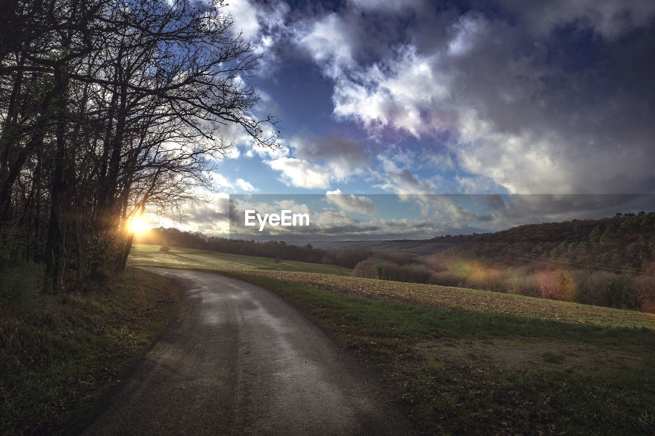 Empty road amidst field against sky