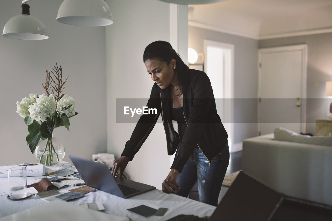 Worried businesswoman looking at laptop while standing by dining table at home office