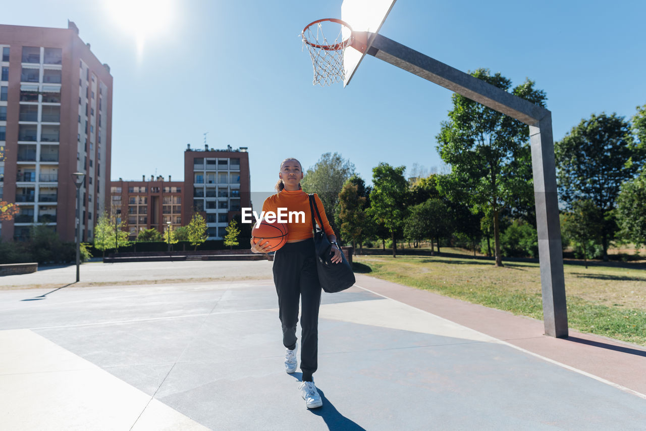 Young sportswoman with basketball walking in sports court