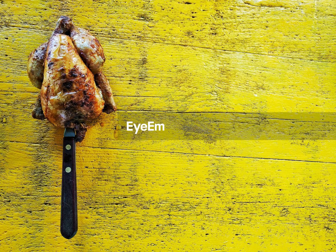 Directly above view of knife in grilled chicken on yellow table