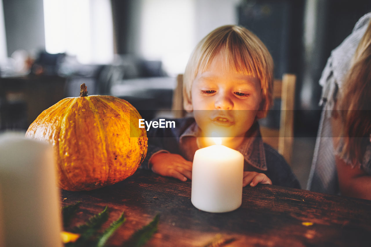 Close-up of boy sitting by candle on table