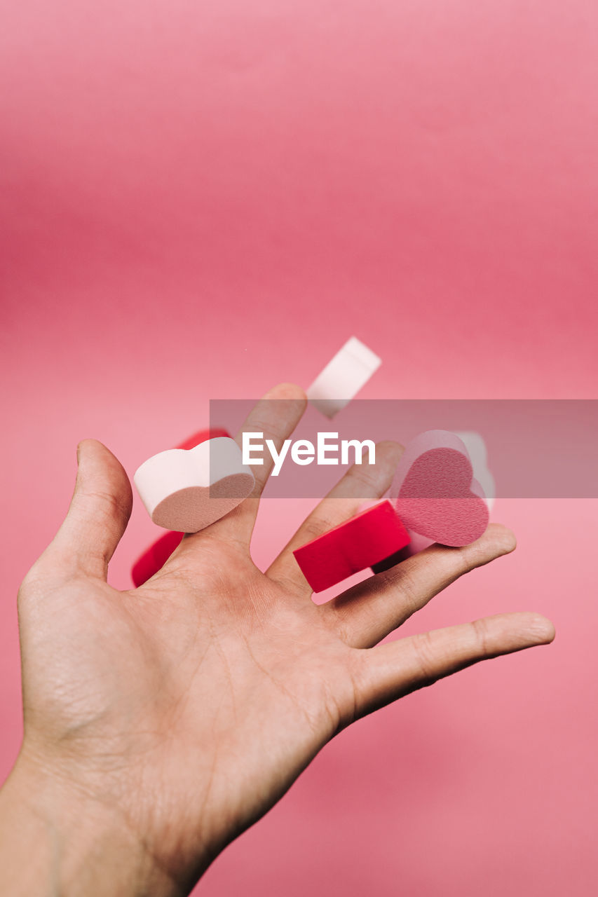 Close-up of woman hand holding heart shape over pink background