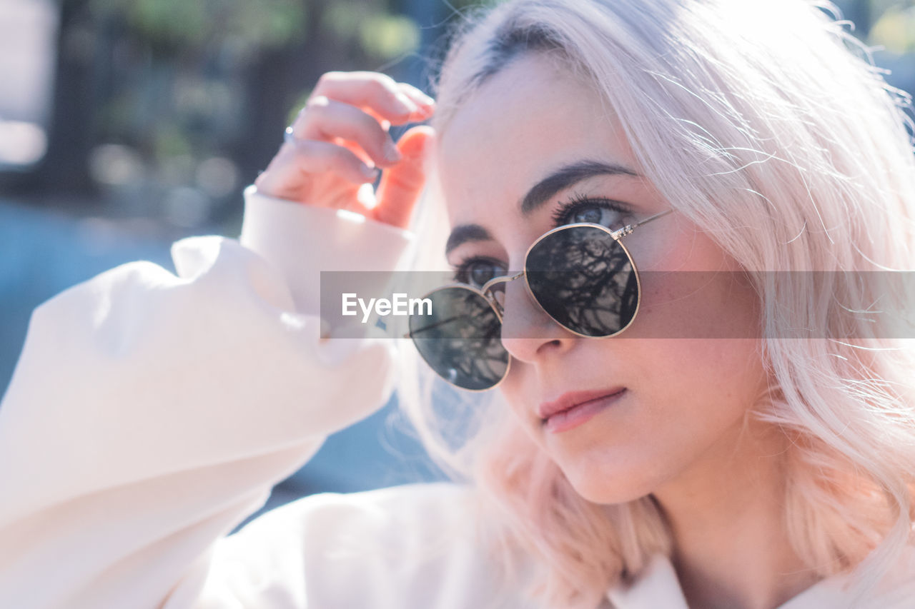 Beautiful young woman wearing sunglasses looking away against tree