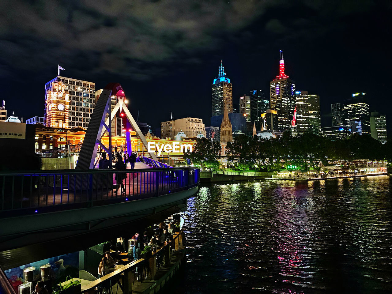 Illuminated melbourne bridge over river by buildings against sky at night