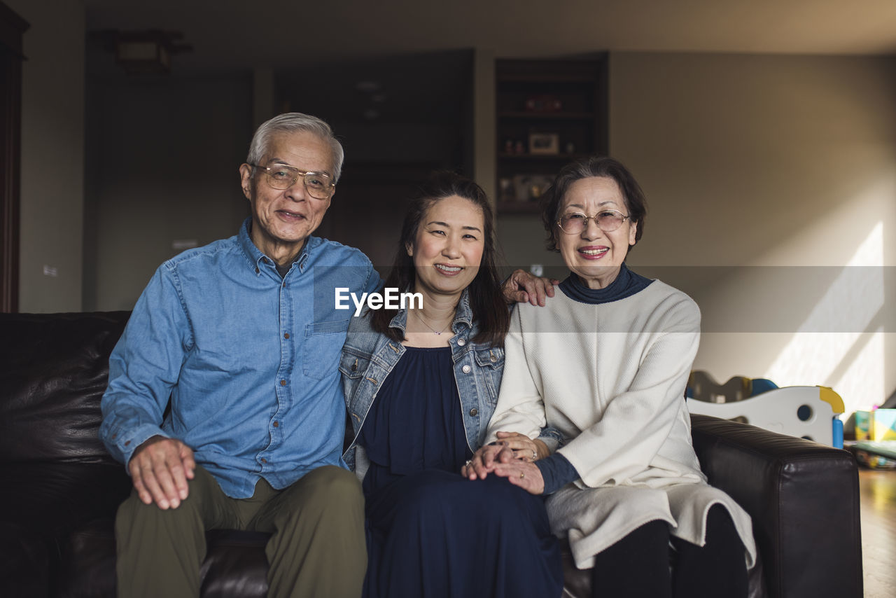 Portrait of adult daughter and her senior parents in living room