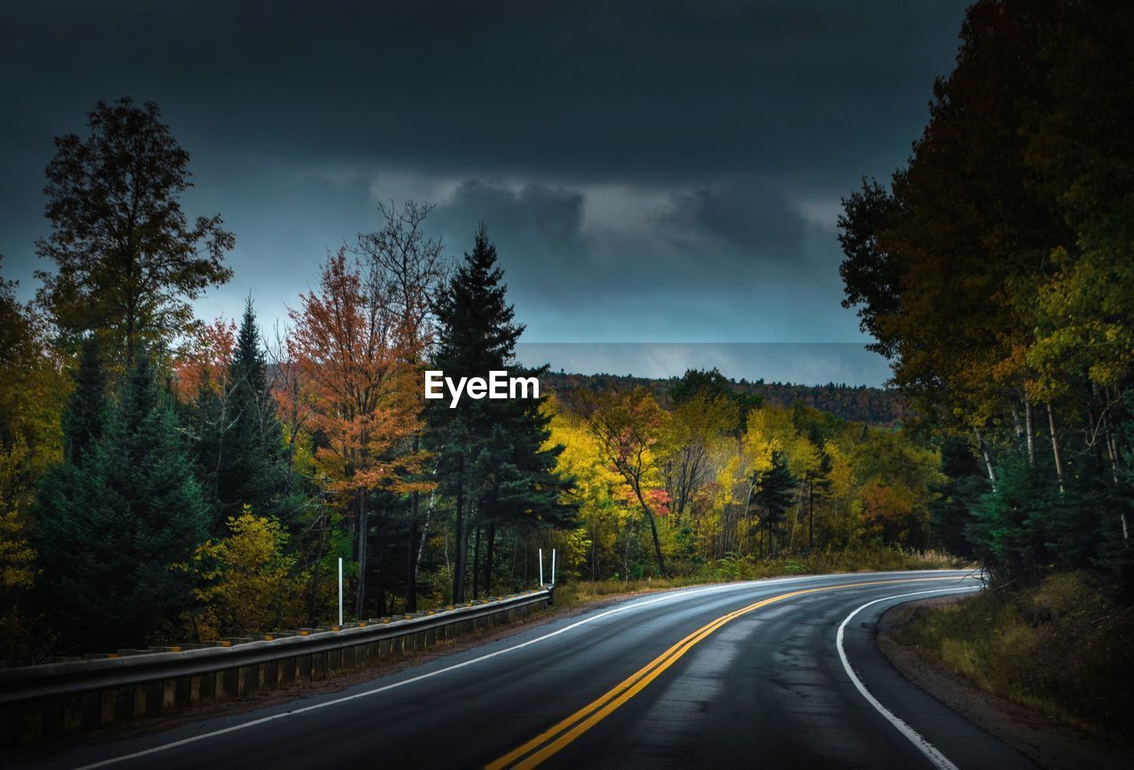 Country road by trees against sky during autumn