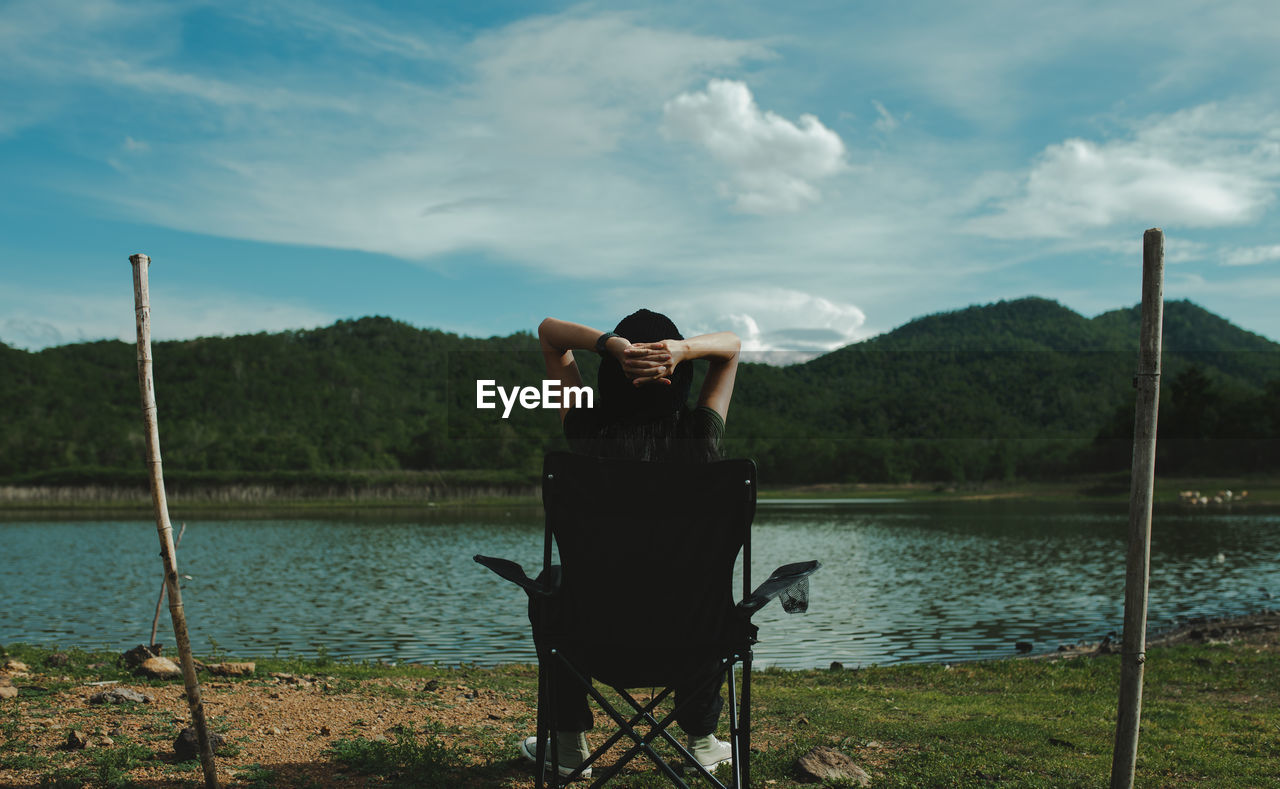 WOMAN SITTING ON LAKE AGAINST SKY