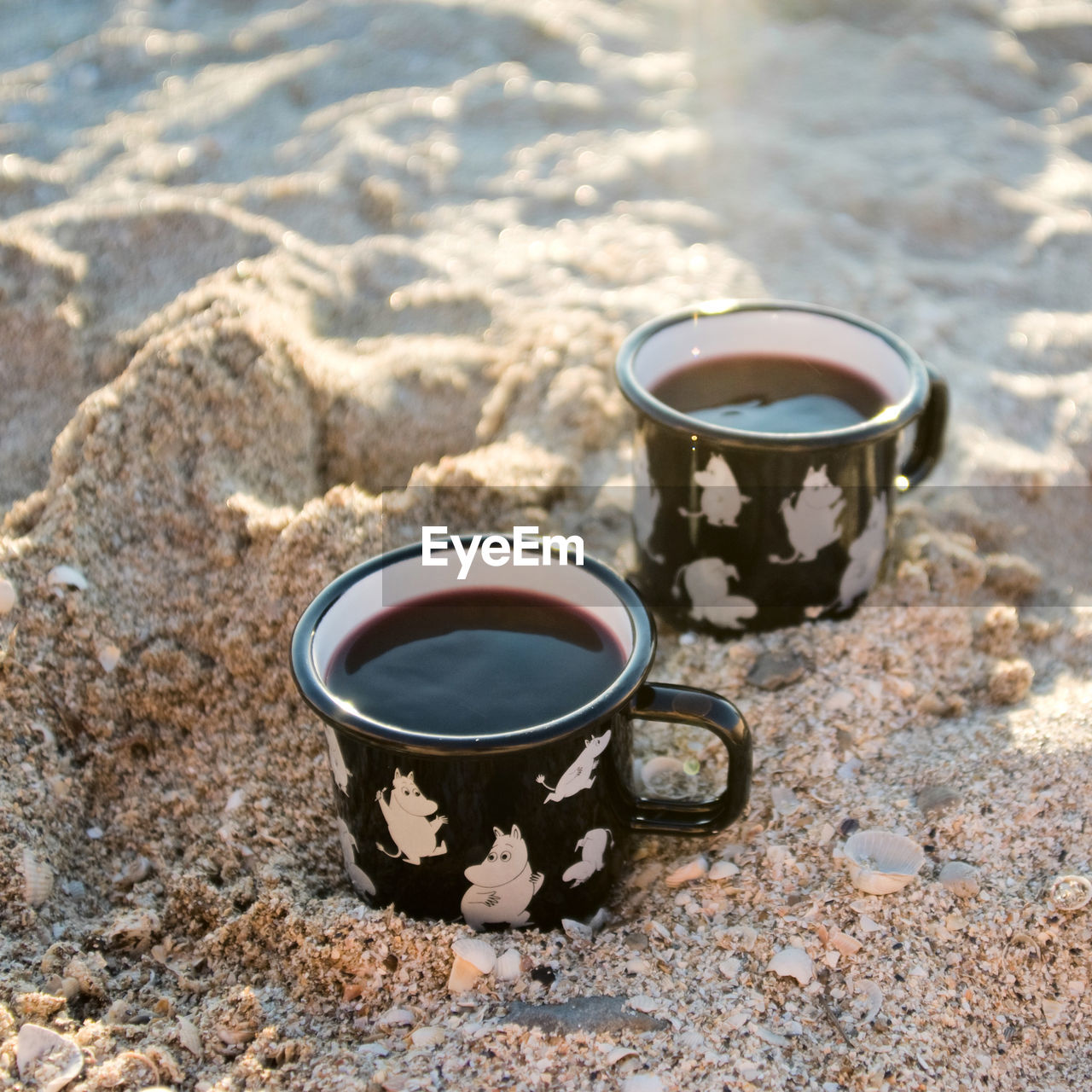 Two enameled cups with coffee/wine on the sand beach