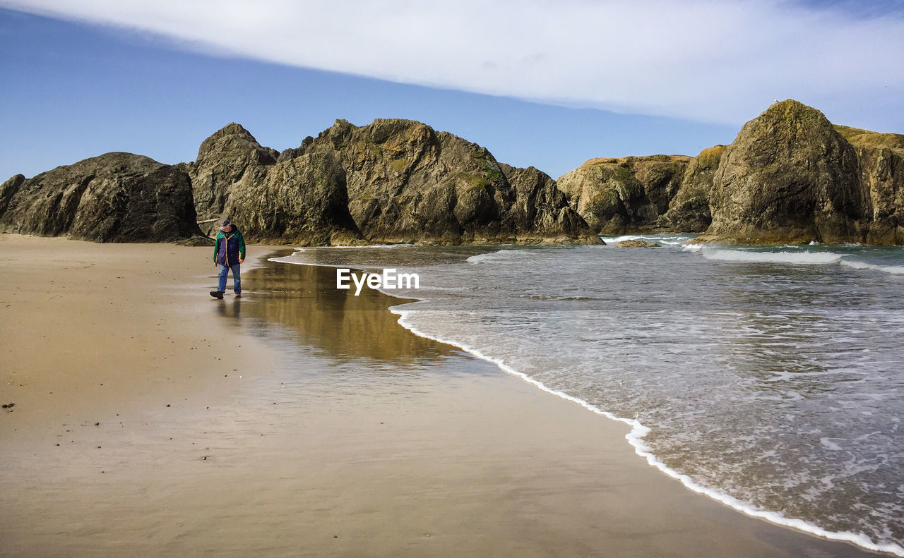 Senior man walking at beach against sky