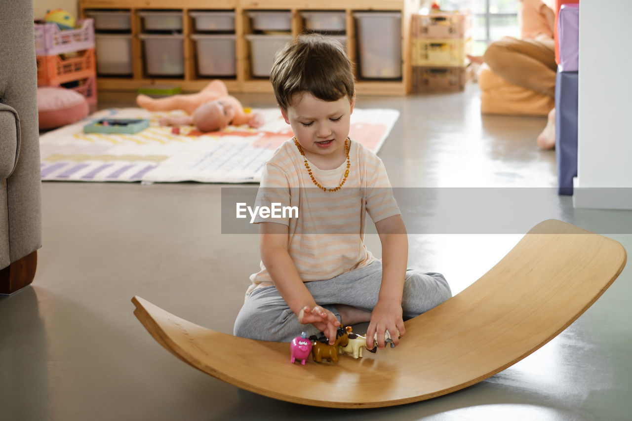 Child playing on balance board for toddlers in kids room. curvy rocker board used for motor physical