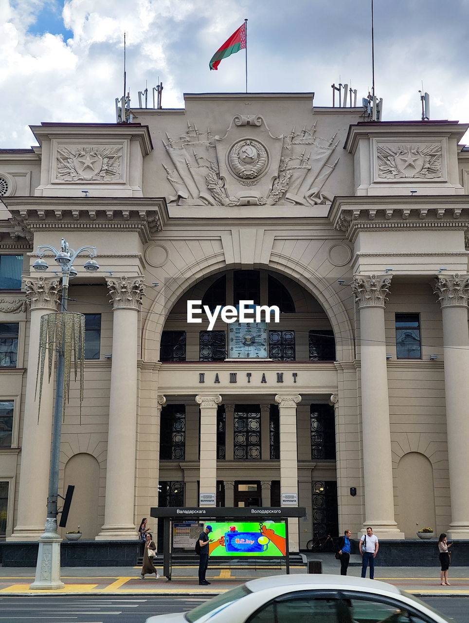 architecture, building exterior, built structure, flag, landmark, city, travel destinations, transportation, car, patriotism, government, travel, building, mode of transportation, arch, cloud, sky, downtown, politics and government, day, vehicle, facade, tourism, nature, history, the past, street, motor vehicle, outdoors