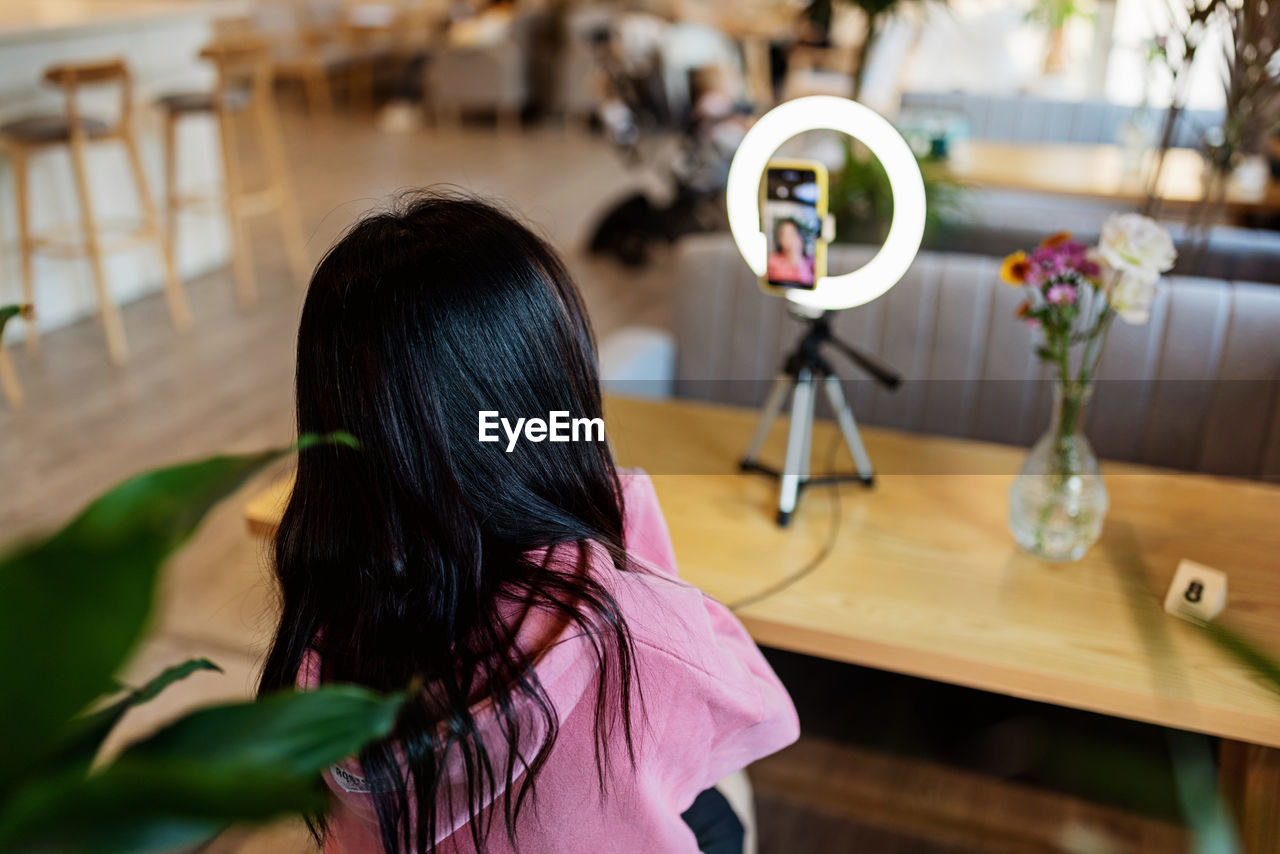 Rear view of woman vlogging at cafe