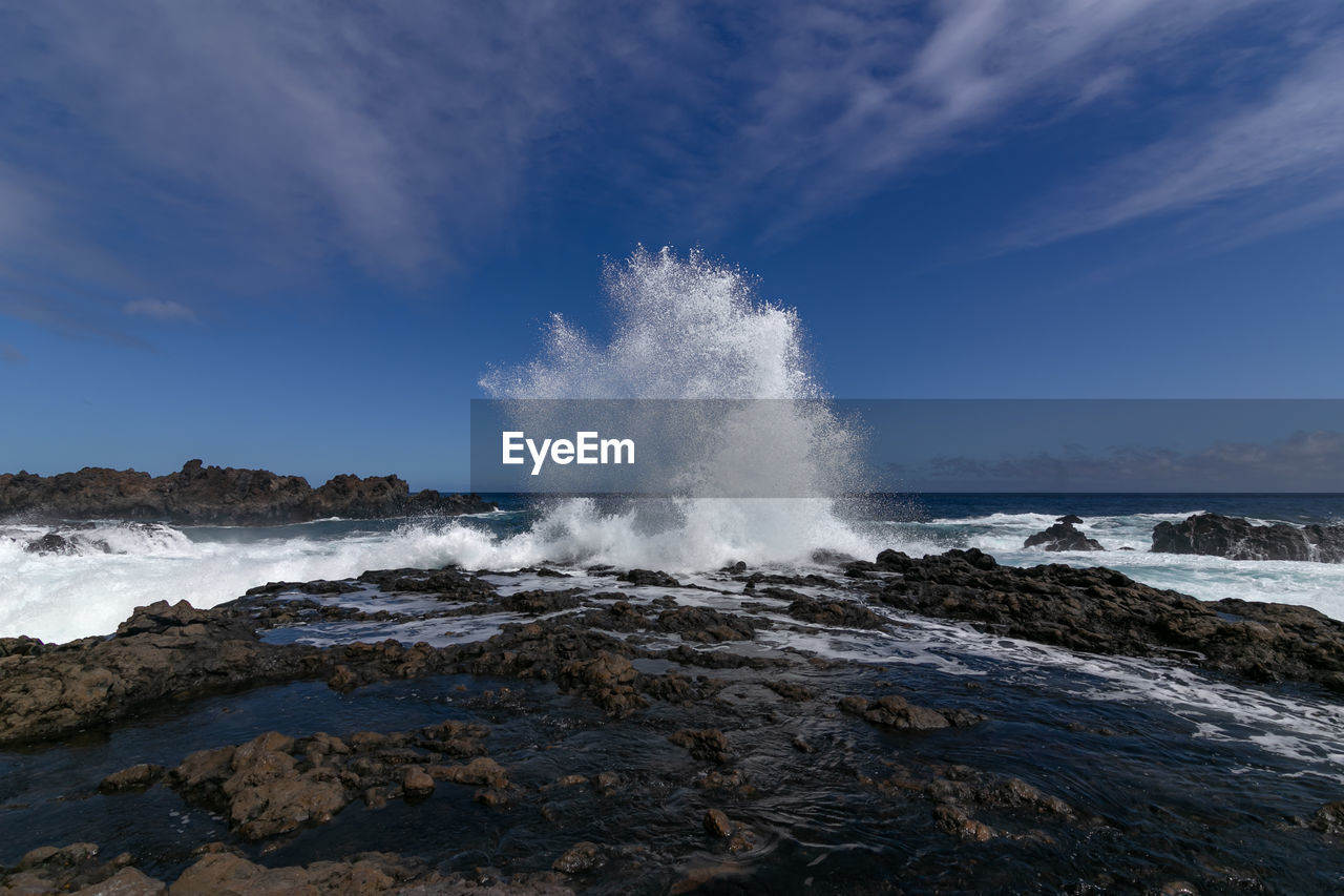 Sea waves splashing on rocks against sky