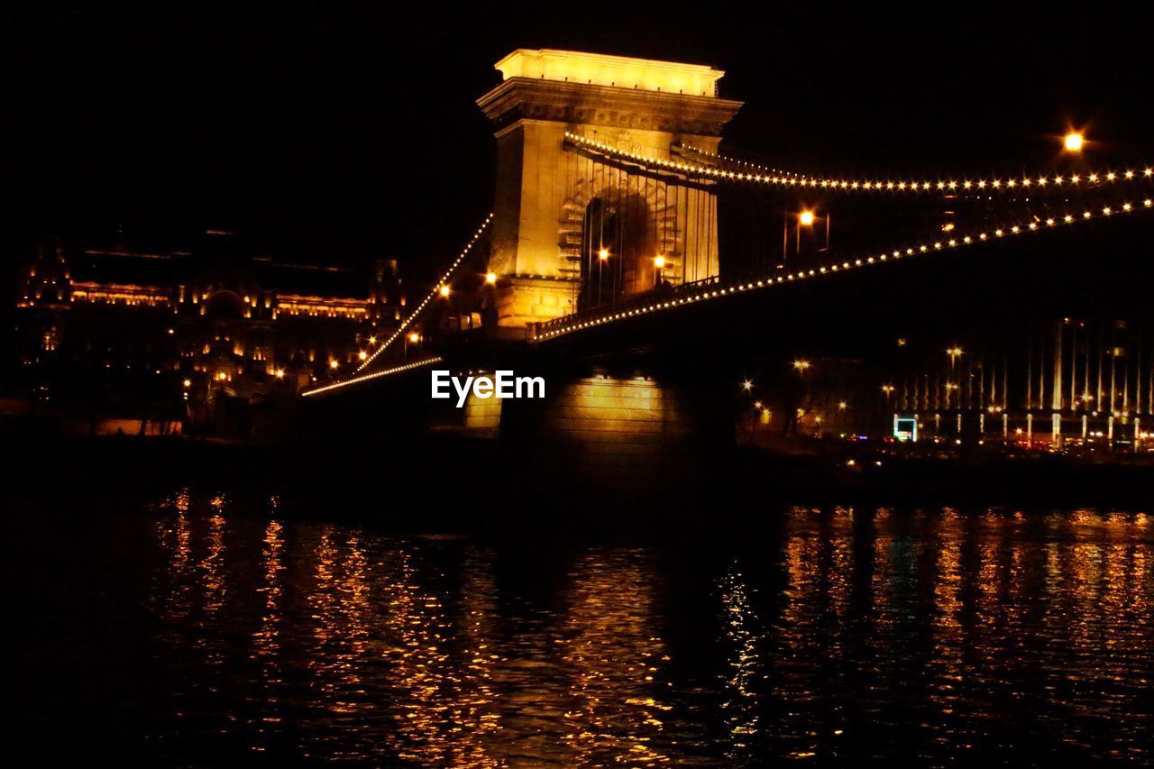 ILLUMINATED BRIDGE OVER RIVER AT NIGHT