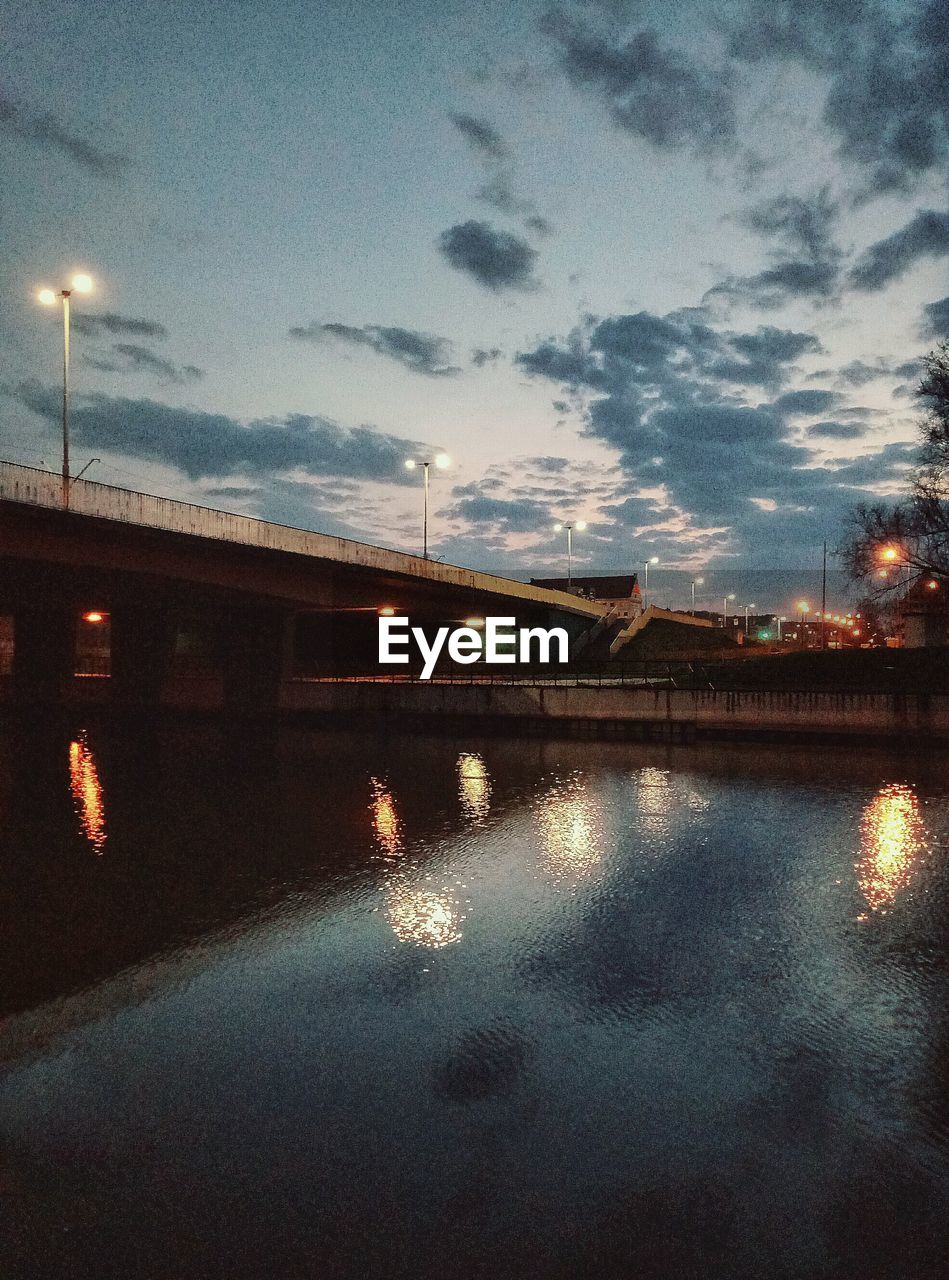 ILLUMINATED BRIDGE OVER RIVER AGAINST SKY IN CITY