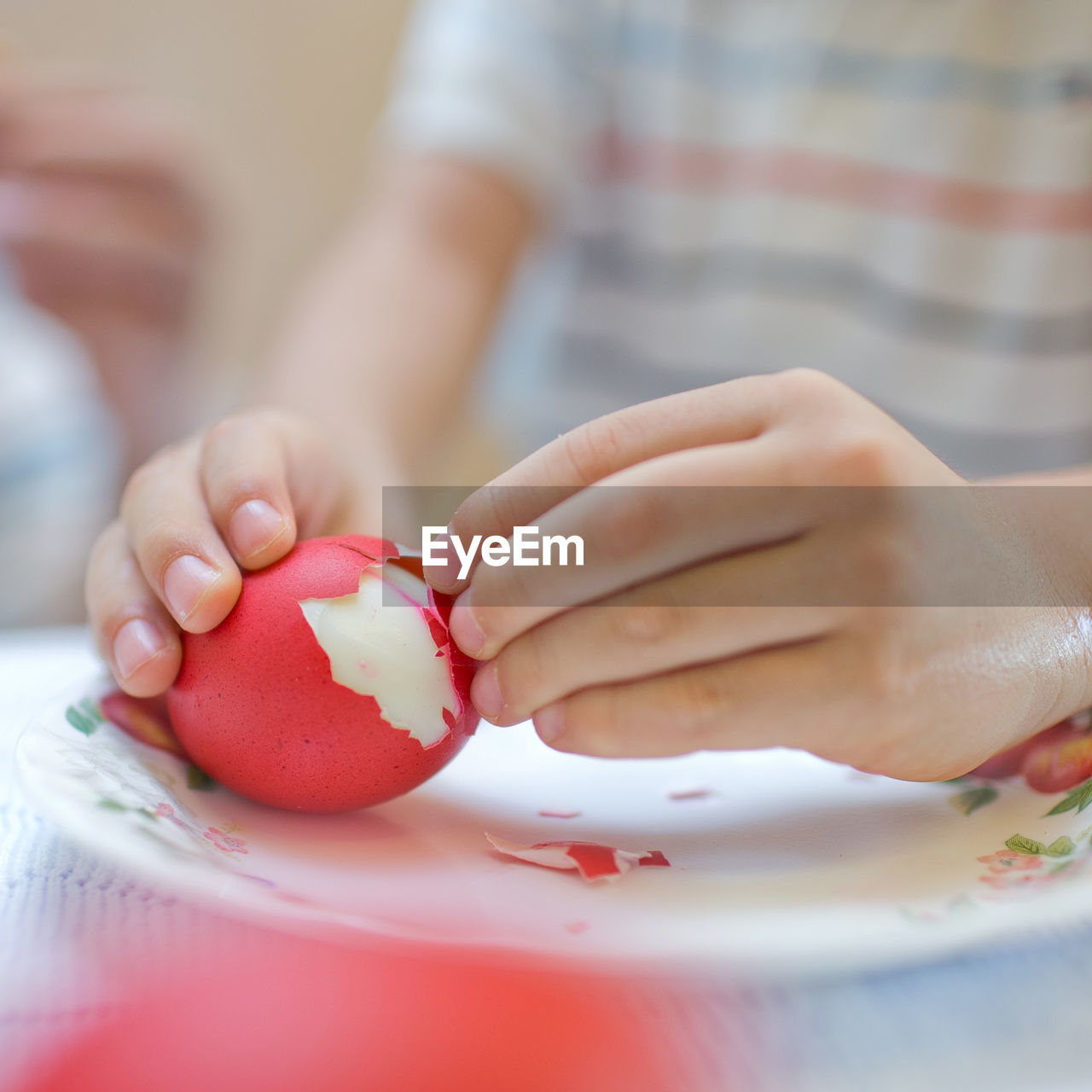 Hands of a child peeling red boiled egg