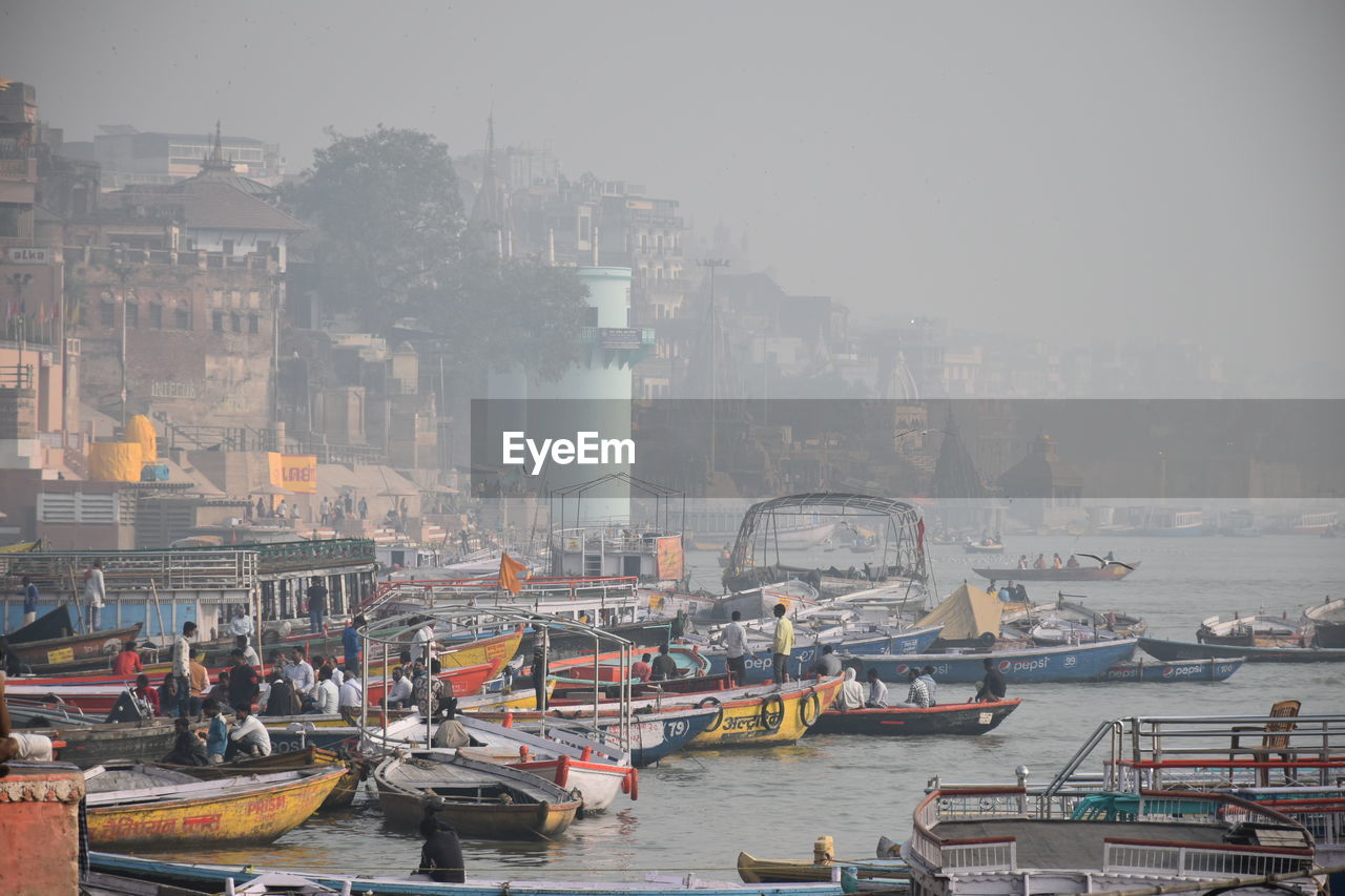 Boats in ganges by buildings in city against sky