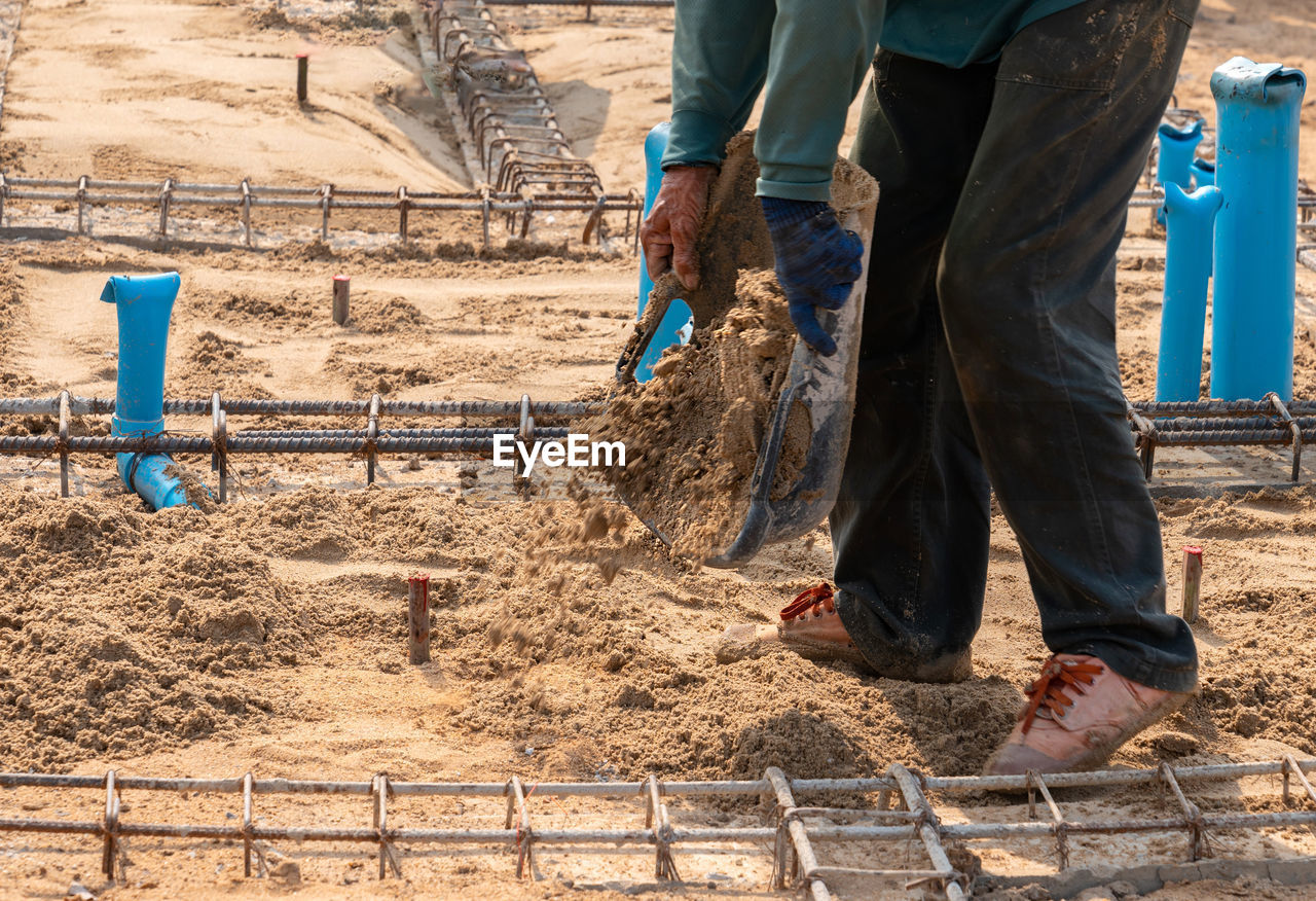 Workers fill the ground with sand to level and prepare for pouring mortar.