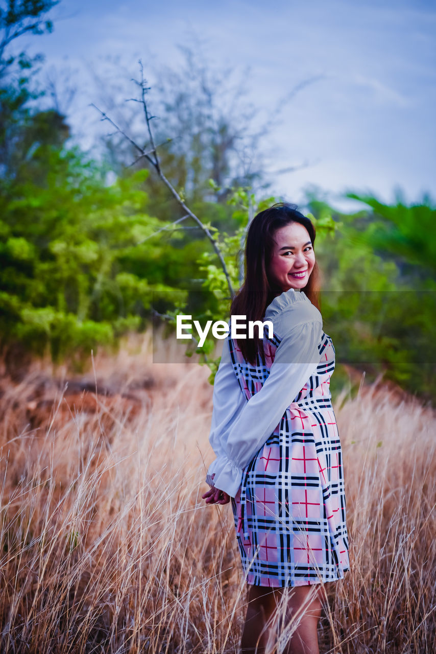 PORTRAIT OF A SMILING YOUNG WOMAN STANDING ON FIELD
