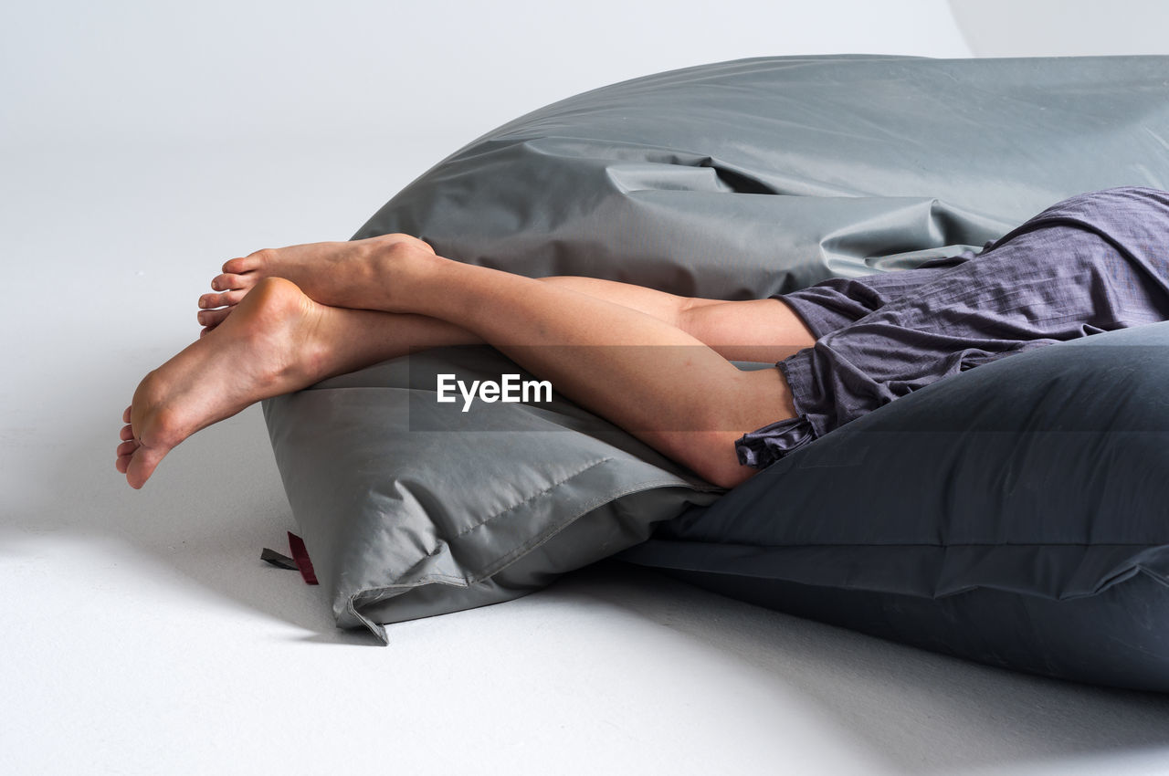 Low section of man relaxing on bed against white background