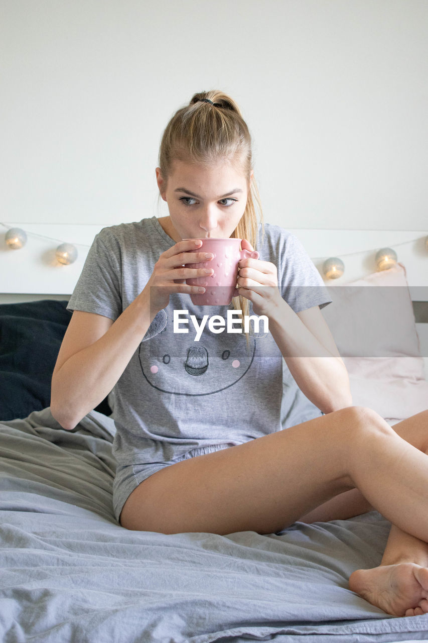 MIDSECTION OF YOUNG WOMAN SITTING ON BED