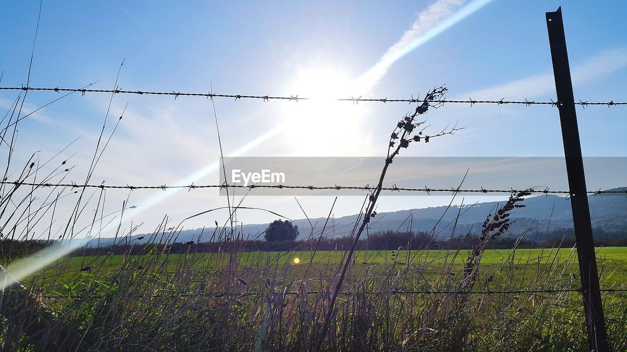 Barbed wire fence on field against sky