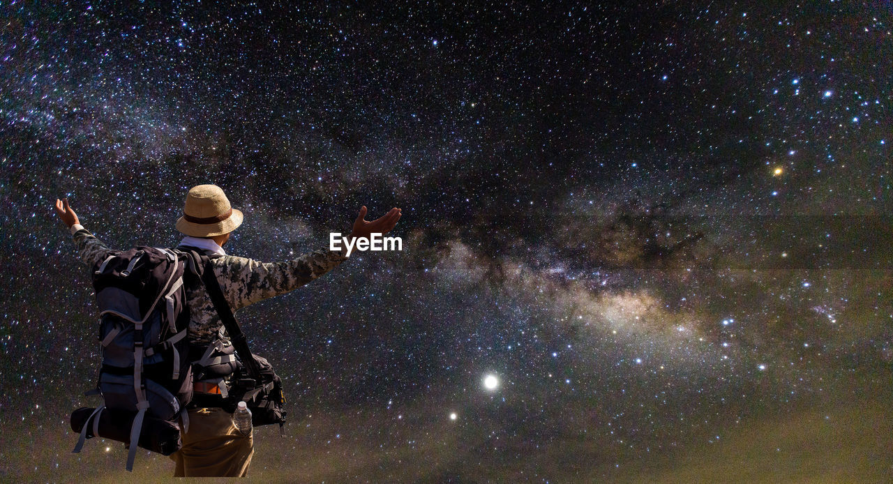 REAR VIEW OF MAN STANDING IN FRONT OF STAR FIELD AGAINST SKY