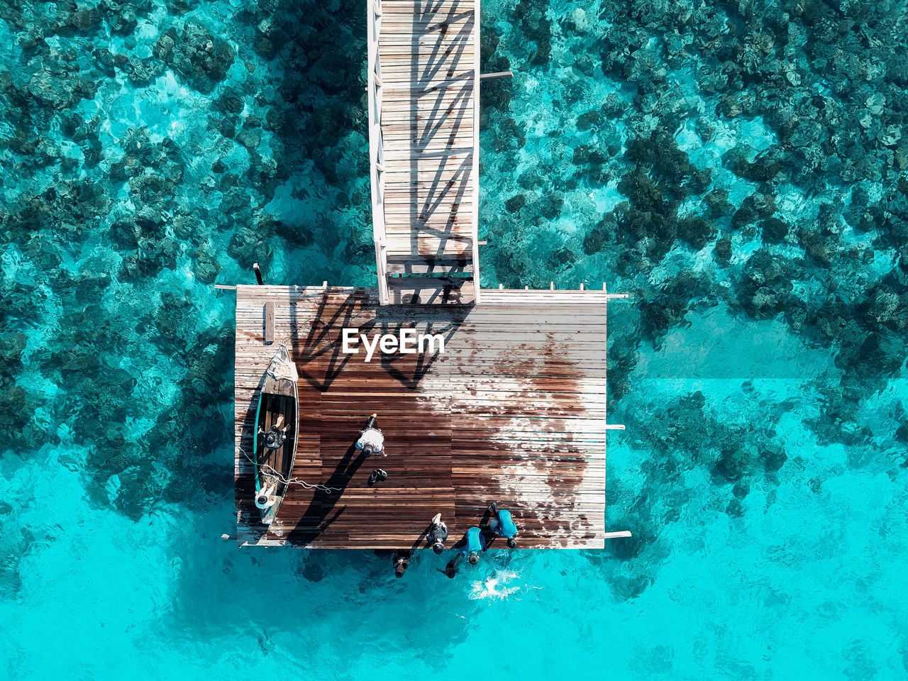 Top down aerial view over the end of wooden jetty with unidentified kids on it.