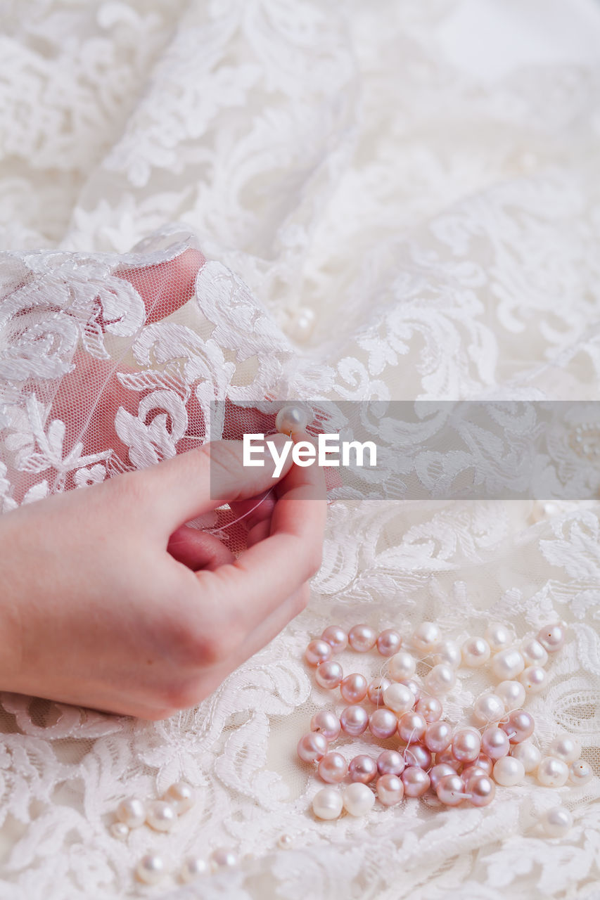 Cropped hand of woman stitching pearls on white wedding dress