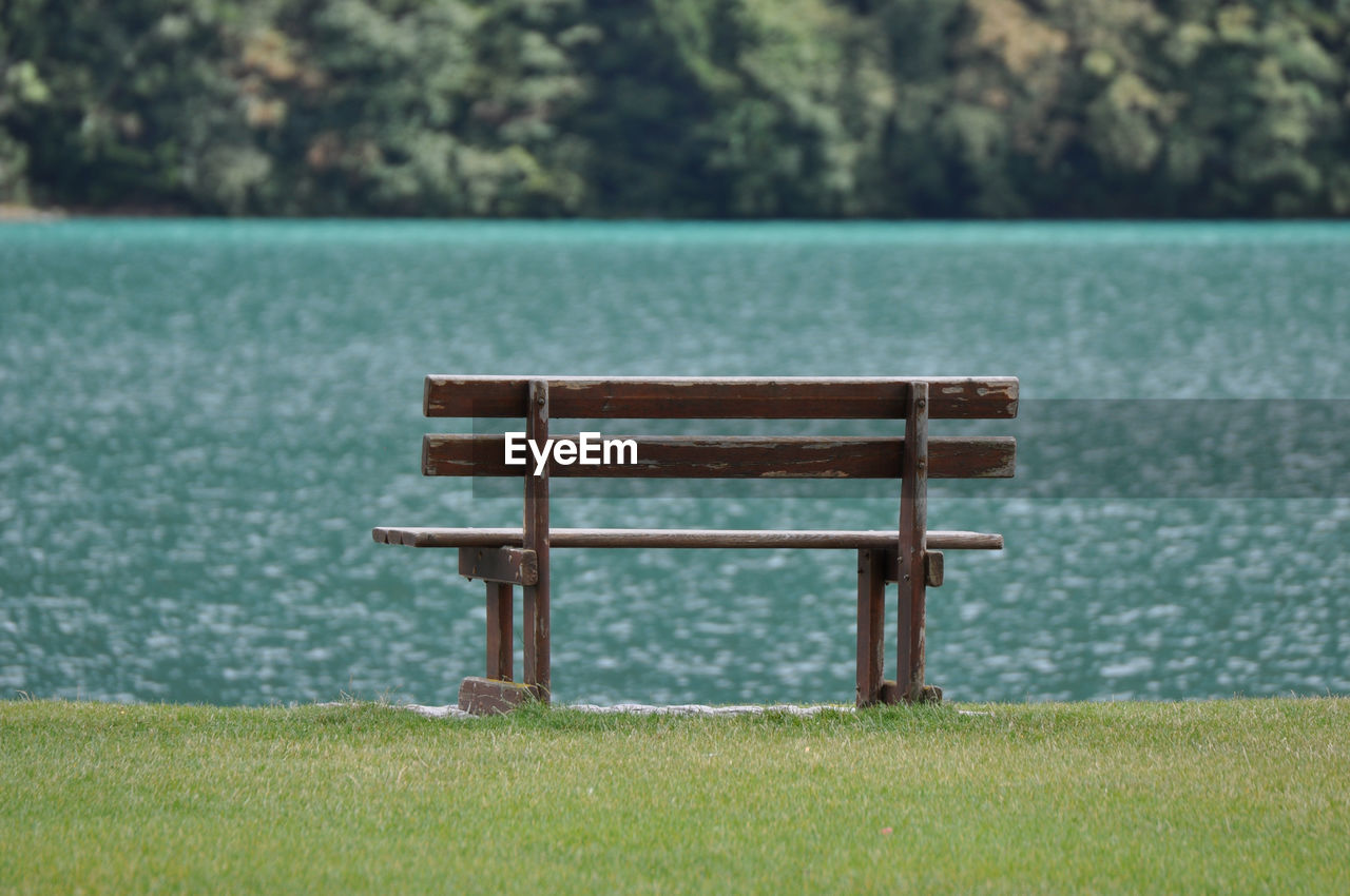 Empty bench on grass against lake at park