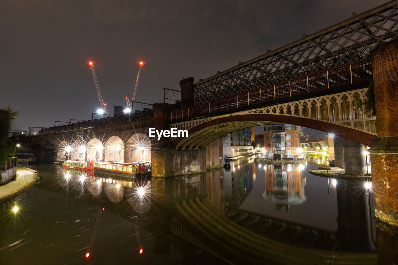 Illuminated bridge long exposure over river in manchester against sky at night