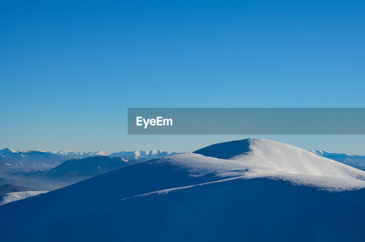 Scenic view of snowcapped mountains against clear blue sky