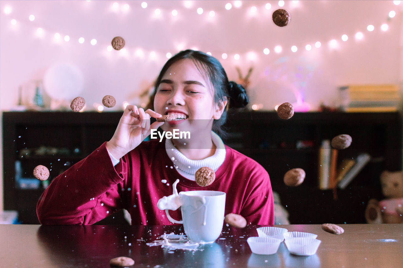 Smiling woman with closed eyes eating cookie at messy table