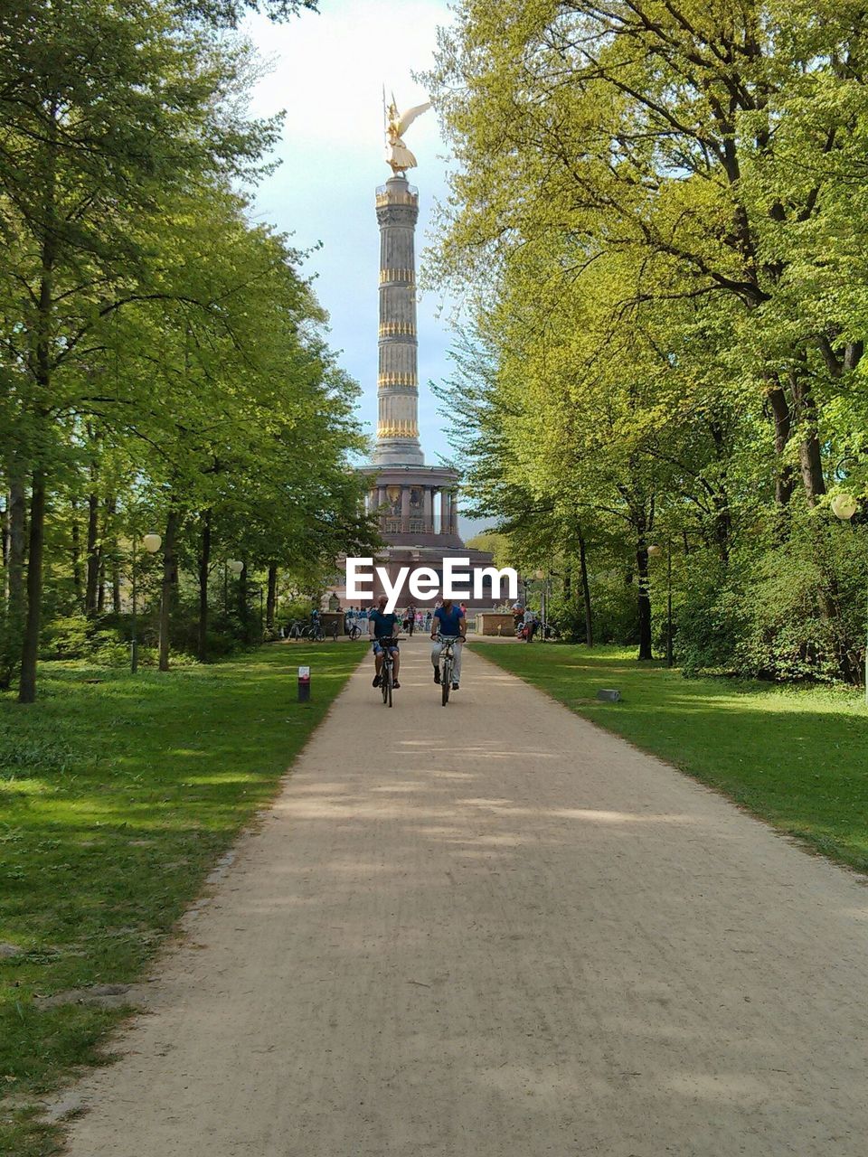 Male friends cycling on walkway in park against berlin victory column