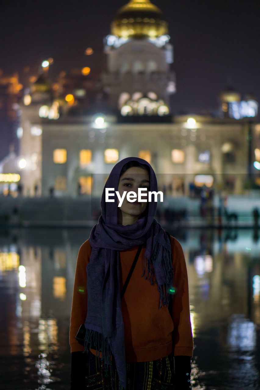 Portrait of woman standing against illuminated temple at night